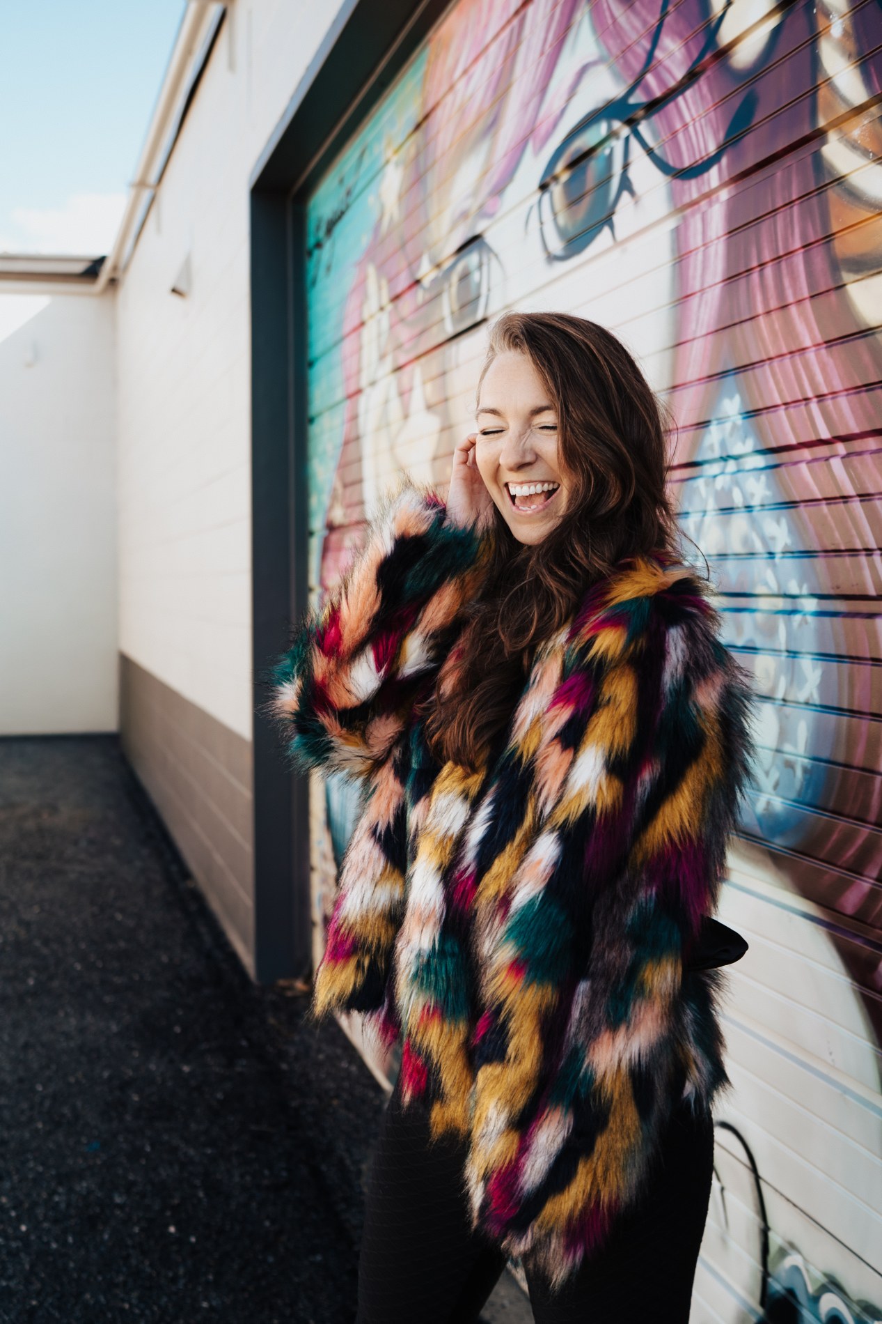 Kimberly laughing in a colorful coat beside a mural