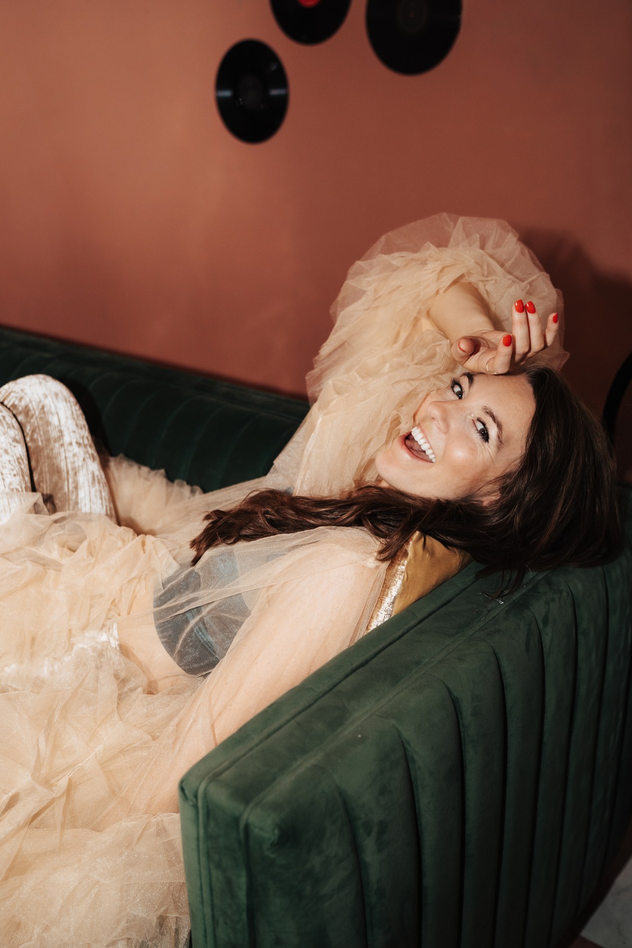 Kimberly reclining on a green sofa in a feathered wrap