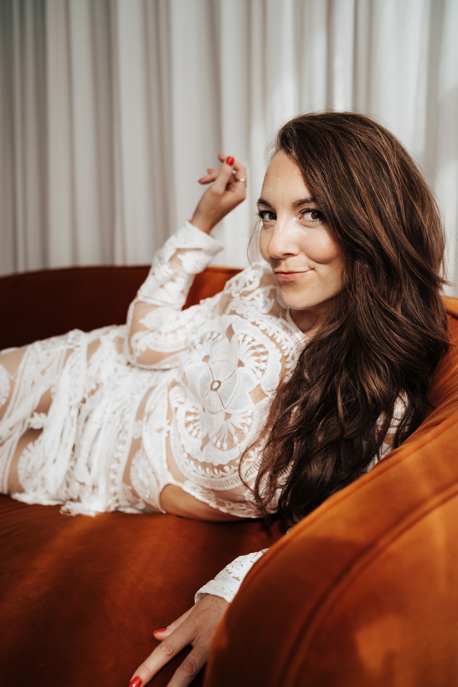 Kimberly relaxing on an orange sofa with a playful smile